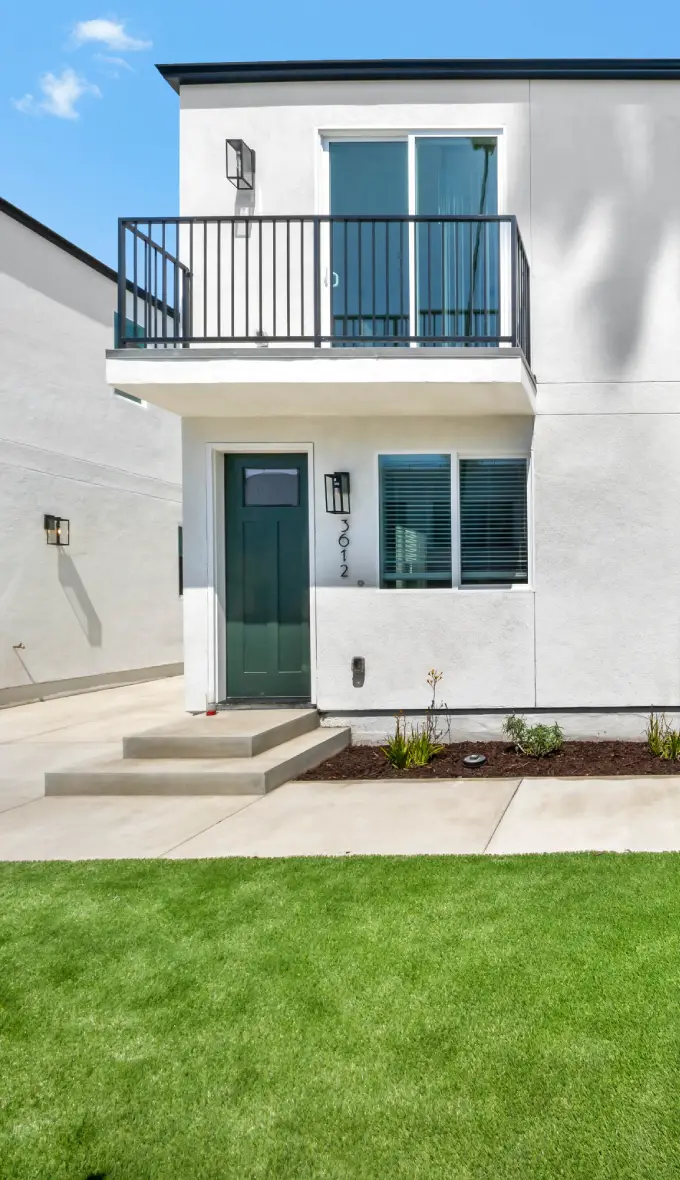 Front exterior view of 36TEN property with white facades, green doors, balconies, and a central walkway lined with palm trees.